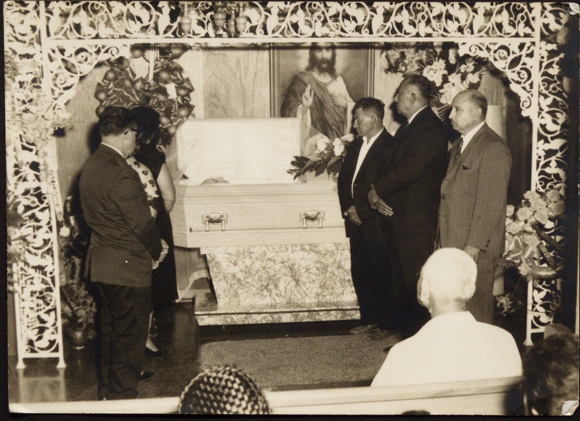 A group of people standing around a coffin

Description automatically generated